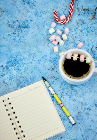 Cup with coffee and marshmallows, blank open notebook with pen on abstract blue background. Top view. Flat mockup. space for text.の写真素材