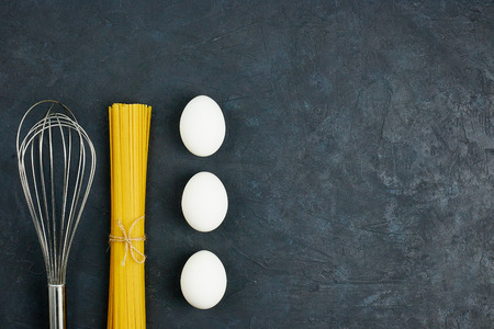 Top view of raw pasta next to an egg and cherry, fresh tomatoes, on a black background.の写真素材
