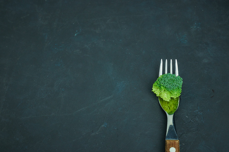 Fresh green broccoli cabbage lies on a fork. Template of healthy food on a dark background. Copy space Top view. Vegetarian food. view from above.の写真素材