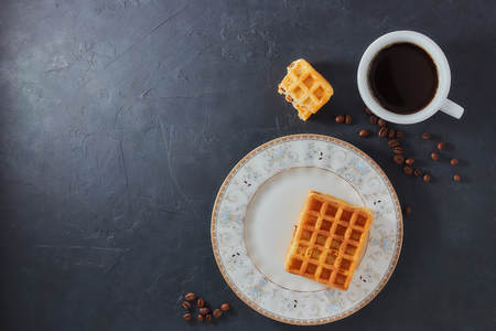 Homemade breakfast, stone black table. Viennese waffles, a cup of coffee, scattered coffee beans, top view, copy spaceの写真素材