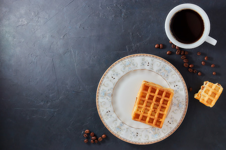 Homemade breakfast, stone black table. Viennese waffles, a cup of coffee, scattered coffee beans, top view, copy spaceの写真素材