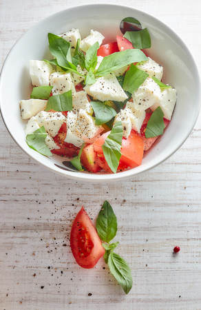 Greek salad with fresh vegetables on a wooden background, feta cheese and basil. Love for healthy raw food concept.の写真素材
