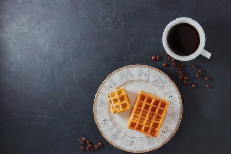 Homemade breakfast, stone black table. Viennese waffles, a cup of coffee, scattered coffee beans, top view, copy spaceの写真素材