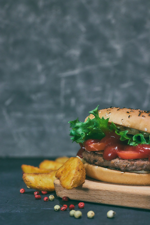 Homemade hamburger with fresh vegetables and potato wedges. On the desk.の写真素材