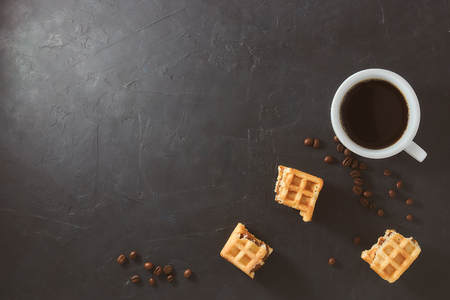 Homemade breakfast, stone black table. Viennese waffles, a cup of coffee, scattered coffee beans, top view, copy spaceの写真素材