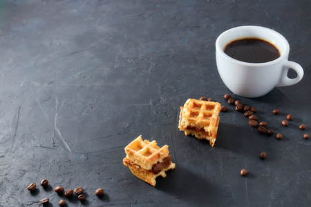 Homemade breakfast, stone black table. Viennese waffles, a cup of coffee, scattered coffee beans, top view, copy spaceの写真素材