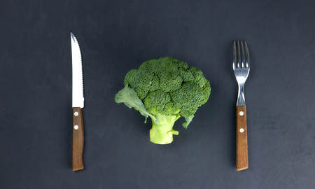 the concept of healthy eating. green, raw broccoli lying on a plate with instruments on a black background. healthy diet. green cabbage close-up. HLS.の写真素材