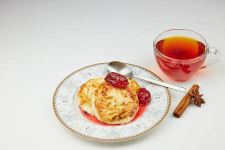 Cheesecakes on a saucer with jam and tea. cottage cheese pancakes or pancakes with strawberry jam and a Cup of tea on a white table. traditional Russian Breakfast.の写真素材