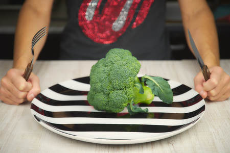 The concept of raw food. Woman eating at the table green raw broccoli.の写真素材