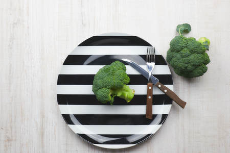 the concept of healthy eating. green, raw broccoli lying on a plate with instruments on a black background. healthy diet. green cabbage close-up. HLS.の写真素材