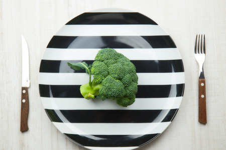 the concept of healthy eating. green, raw broccoli lying on a plate with instruments on a black background. healthy diet. green cabbage close-up. HLS.の写真素材