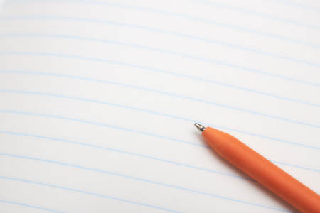 orange ballpoint pen lies on a white sheet of paper close-up. concept of education. place for text.の写真素材