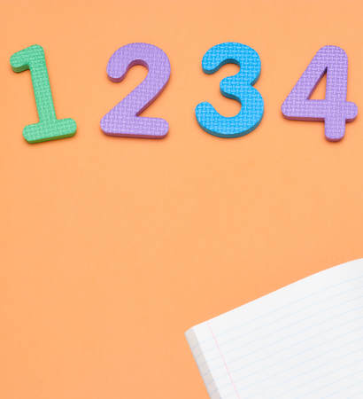 Notebook, pen and colored numbers on orange background. Accessories for study. Mathematics,, flat, copy spaceの写真素材