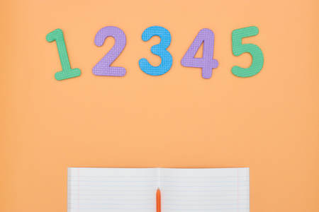 Notebook, pen and colored numbers on orange background. Accessories for study. Mathematics,, flat, copy spaceの写真素材