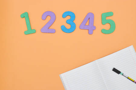 Notebook, pen and colored numbers on orange background. Accessories for study. Mathematics,, flat, copy spaceの写真素材
