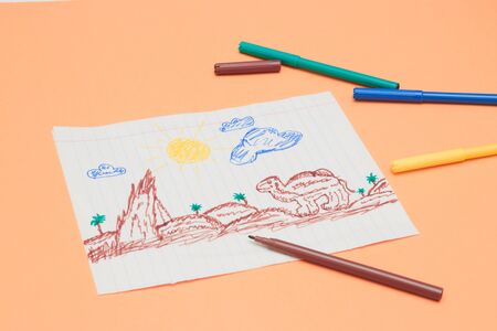 Next to the markers is a primitive children's drawing with a felt-tip pen on a peach background. child development. children learn to draw.のeditorial素材