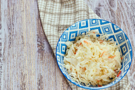 salad of pickled cabbage. Traditional Russian appetizer sauerkraut with carrots in a plate on a white wooden table. Rustic style. Selective focus and copy spaceの写真素材