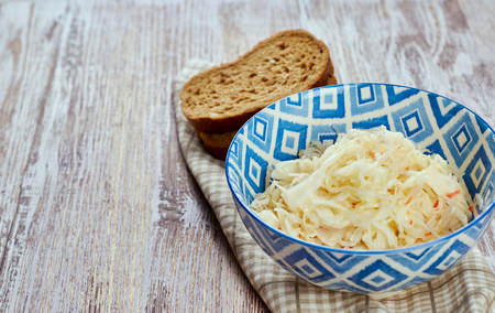 salad of pickled cabbage. Traditional Russian appetizer sauerkraut with carrots in a plate on a white wooden table. Rustic style. Selective focus and copy spaceの写真素材