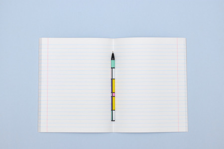 open school notebook with pen on blue background. a clean, white sheet of notebook paper for recording.の写真素材