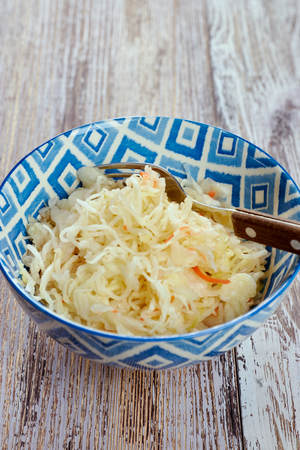 salad of pickled cabbage. Traditional Russian appetizer sauerkraut with carrots in a plate on a white wooden table. Rustic style. Selective focus and copy spaceの写真素材