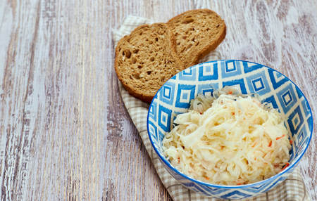 salad of pickled cabbage. Traditional Russian appetizer sauerkraut with carrots in a plate on a white wooden table. Rustic style. Selective focus and copy spaceの写真素材