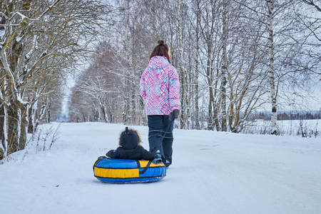 Mom rolls her little son on tubing in the Park in the winter. Happy family outdoors.の写真素材