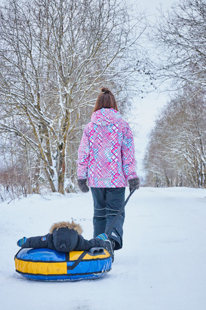 Mom rolls her little son on tubing in the Park in the winter. Happy family outdoors.の写真素材