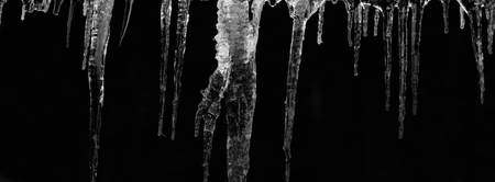 number of natural icicles on a black background. frozen water in winter. a group of dangling icicles. copy space.の写真素材