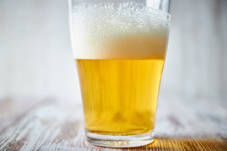 A glass of light beer with foam on a wooden background, close-up. vertical view of the glass.の写真素材