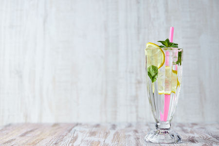 Lemonade with ice, lemon slices and mint in a glass with straw on a light wooden background. copy space. summer, refreshing drink.の写真素材