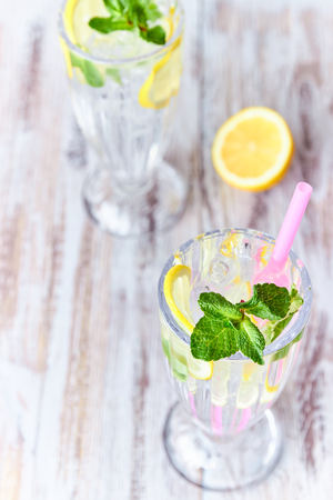 Lemonade with ice, lemon slices and mint in a glass with straw on a light wooden background. copy space. summer, refreshing drink.の写真素材