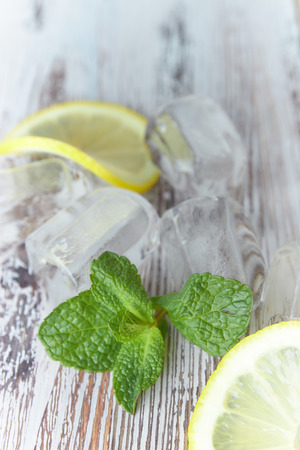 pieces of lemon with ice cubes on an old wooden table close-up. sliced lemon with mint.の写真素材