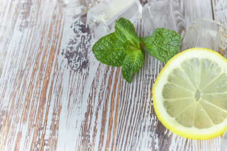 pieces of lemon with ice cubes on an old wooden table close-up. sliced lemon with mint.の写真素材