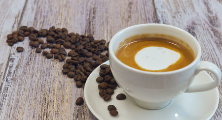 white cup with black coffee with milk. Handful of coffee beans on a wooden table. horizontal view of a cup with a coffee drink. Copy space close up.の写真素材