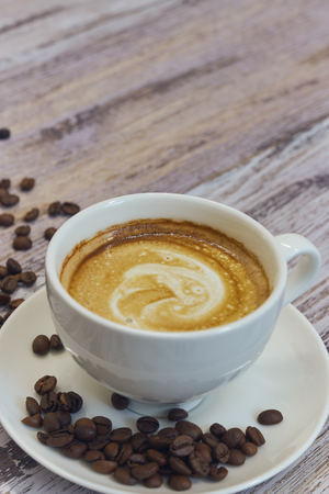 white cup with black coffee with milk. Handful of coffee beans on a wooden table. vertical view of drink with coffee. Copy space close up.の写真素材