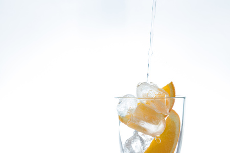 ice drink with orange and ice in the studio on a white background. a stream of water pours intoの写真素材