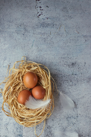 Top view of three brown chicken eggs in a nest of straw on gray concrete. Plenty of room for text. Copy spaceの写真素材