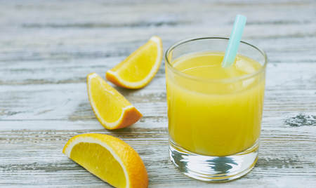 a glass of fresh orange juice with fresh citrus fruits on a light wooden table. horizontal view.の写真素材