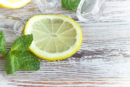 pieces of lemon with ice cubes on an old wooden table close-up. sliced lemon with mint.の写真素材