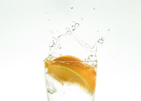 Slice the orange slice in a glass of water and make a spray on a white background. water spray in the air.の写真素材