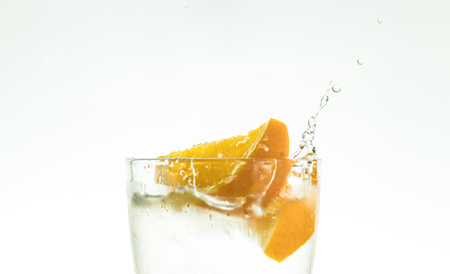 Slice the orange slice in a glass of water and make a spray on a white background. water spray in the air.の写真素材