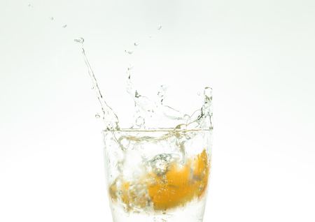 Slice the orange slice in a glass of water and make a spray on a white background. water spray in the air.の写真素材