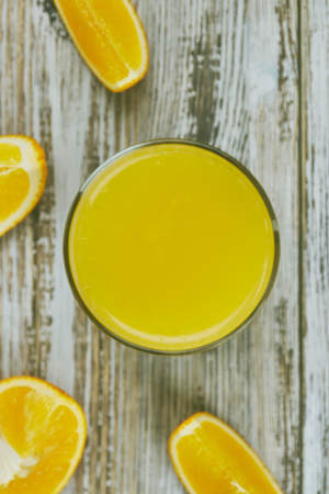 A glass of fresh orange juice and orange fruits on a wooden table. vertical view close-up. refreshingの写真素材