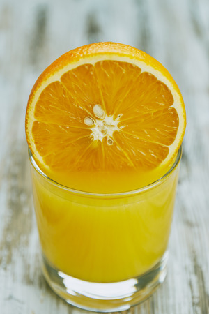 A glass of fresh orange juice and orange fruits on a wooden table. vertical view close-up. refreshingの写真素材
