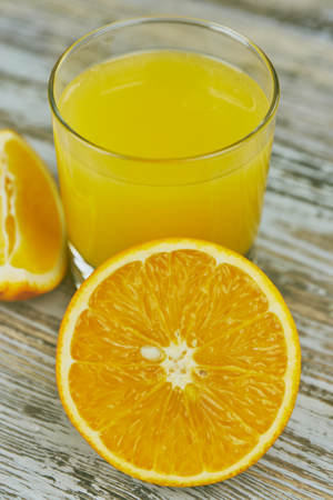 A glass of fresh orange juice and orange fruits on a wooden table. vertical view close-up. refreshingの写真素材