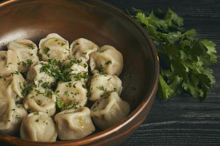 pelmeni with butter and greens on a black wooden table. Russian traditional dish of dough and minced meat. close up photo.の写真素材