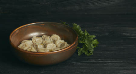 pelmeni with butter and greens on a black wooden table. Russian traditional dish of dough and minced meat. close up photo.の写真素材
