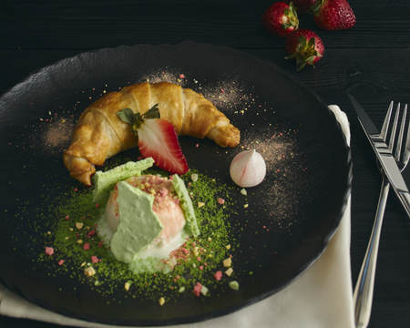 Slice of apple strudel with a scoop of vanilla ice cream on a black plate, on a wooden black table, decorated with meringue and strawberries. close-up. horizontal view of bakedの写真素材