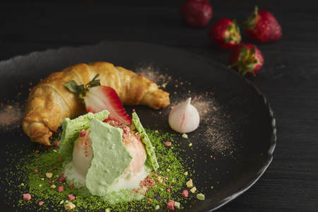 Slice of apple strudel with a scoop of vanilla ice cream on a black plate, on a wooden black table, decorated with meringue and strawberries. close-up. horizontal view of bakedの写真素材