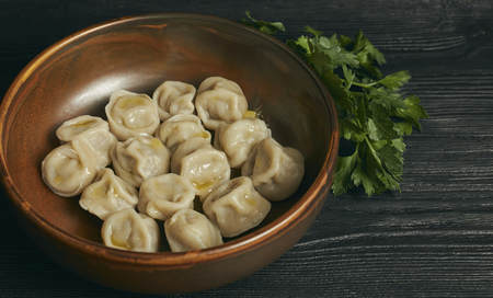 pelmeni with butter and greens on a black wooden table. Russian traditional dish of dough and minced meat. close up photo.の写真素材